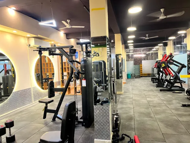 A cable machine station beside a round backlit mirror, with a tiled gym floor stretching past a row of weight machines and treadmills.