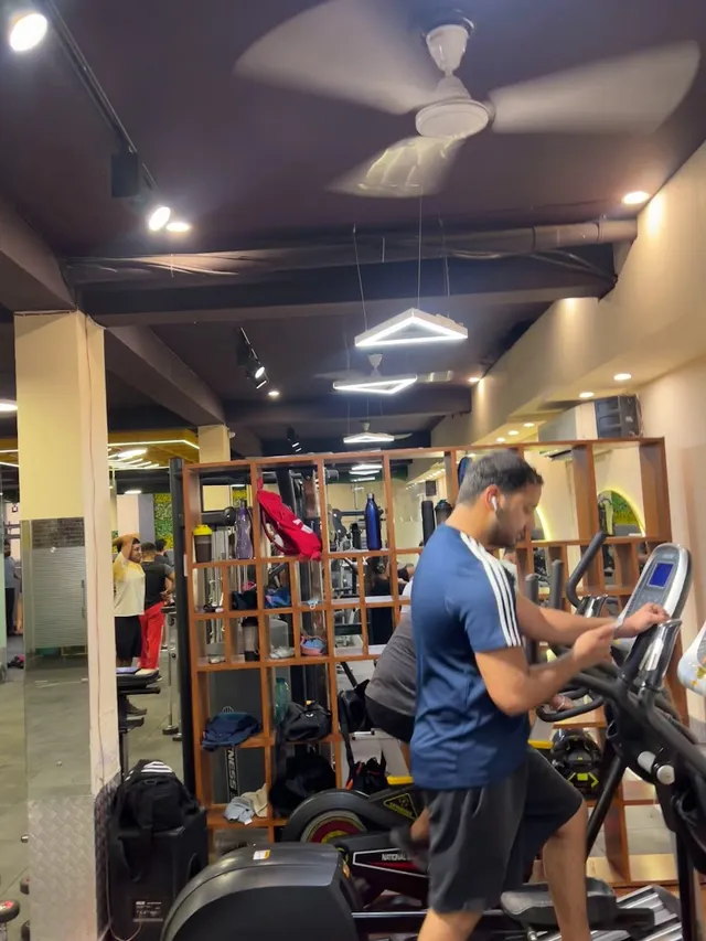 A member using a treadmill on the gym floor, with wooden cubby shelving, ceiling fans and pendant lighting overhead.